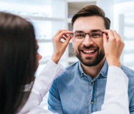 Young female doctor ophthalmologist is helping handsome man to choose the most appropriate eyeglasses. Doctor and patient in modern ophthalmology clinic